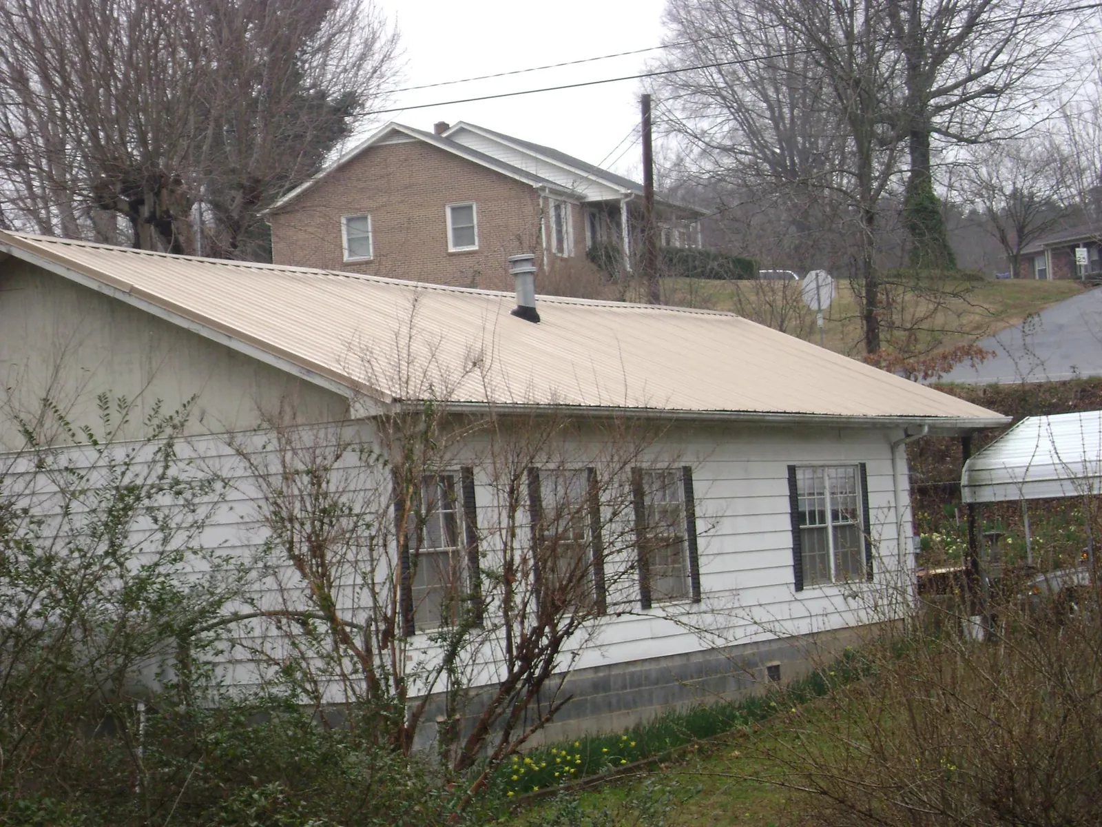 Tan metal roof on a white sided house set into a hillside — Commercial Roofing by Roofing Brothers in Fanwood